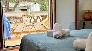 A room with a bed, a table with a vase, and a view of an outdoor area with a table and chairs. - Very cosy Townhouse 5 minutes walking to the beach  (Pals)