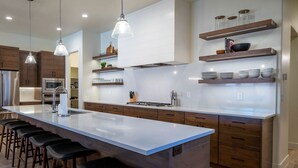 A modern kitchen with a large island, bar stools, wooden cabinets, and pendant lighting. - Arcadia 66 + 67 | TWO POOLS + HOT TUBS + ARCADES + POOL TABLES (Santa Clara)