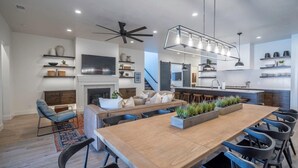 A modern kitchen with a central island, a dining area with a long table and chairs, a sofa, and a fireplace. - Arcadia 66 + 67 | TWO POOLS + HOT TUBS + ARCADES + POOL TABLES (Santa Clara)
