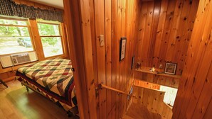 A wooden-paneled room with a bed, a window, a radiator, and a small shelf with items.