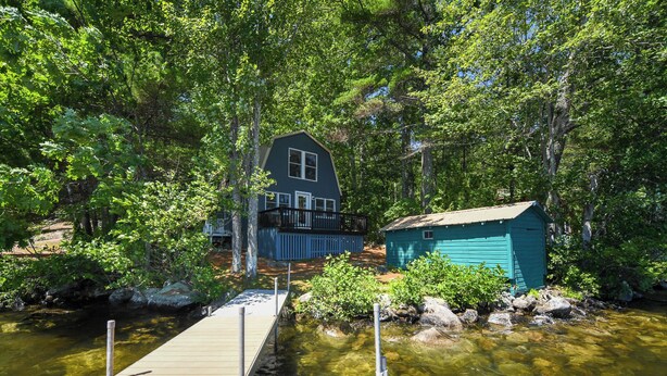 A house with a dock extending into a river surrounded by dense trees.