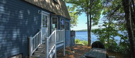 A cabin with a porch, a picnic table, and a view of a lake.