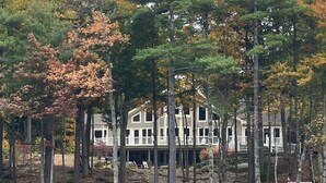 Een pand aan het water met een huis van twee verdiepingen, een steiger en omliggende bomen.