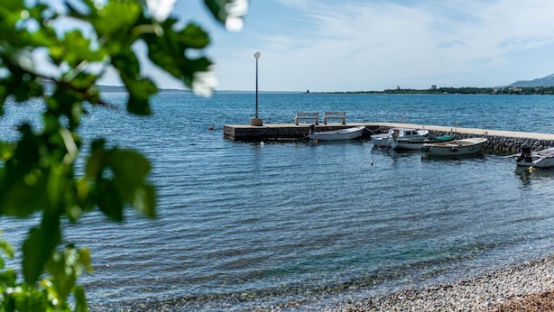 Ein ruhiger See mit Steg, Booten und einer Laterne.