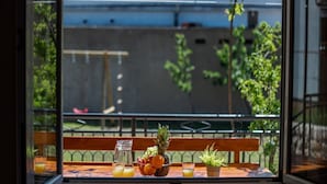 Ein Tisch mit Obstschale, Gläsern und einer Karaffe auf einem Balkon mit Blick auf ein Gebäude und Grünflächen.
