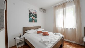 Ein Hotelzimmer mit einem hölzernen Bett, weißer Bettwäsche, einem Nachttisch mit Lampe und einem Gemälde von einer Berglandschaft.