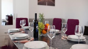 Une table à manger dressée avec des assiettes, des verres et une bouteille de vin, ainsi qu’un panier de fruits et un ananas posés sur la table.