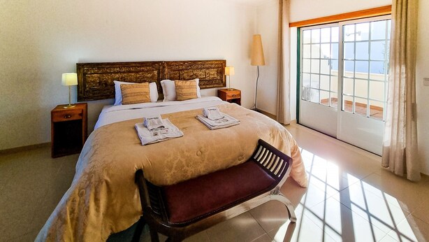 Une chambre d’hôtel avec un grand lit, un banc, une table de chevet, une lampe et une vue sur l’extérieur.