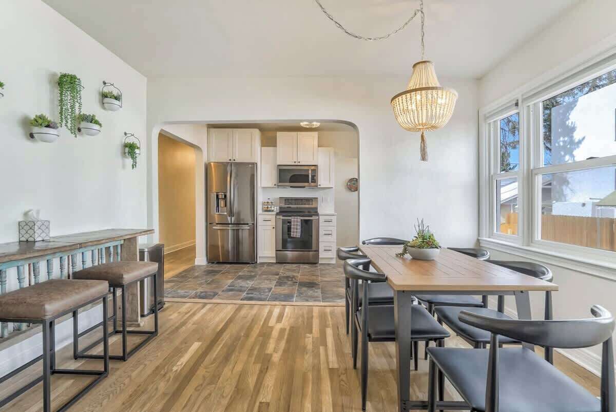 Une cuisine moderne avec des meubles blancs, des appareils en acier inoxydable et une table à manger en bois, assortie de chaises noires.