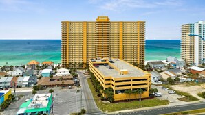 A large yellow hotel with multiple floors and a parking garage, located near a beach with clear blue water.