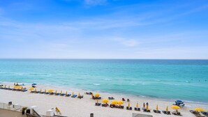 A beach with rows of sun loungers and umbrellas, a clear sky, and calm sea.