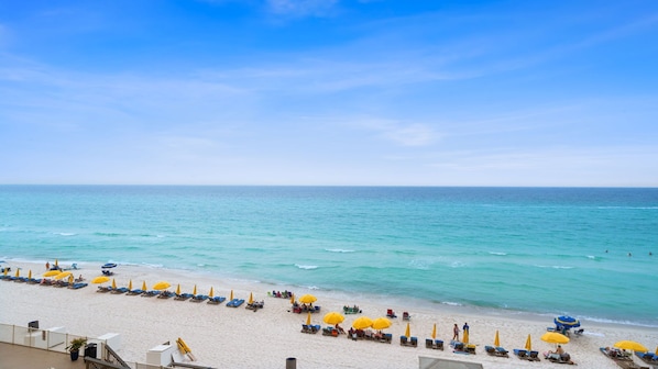 Une plage bordée de rangées de transats et de parasols, un ciel dégagé et une mer calme.