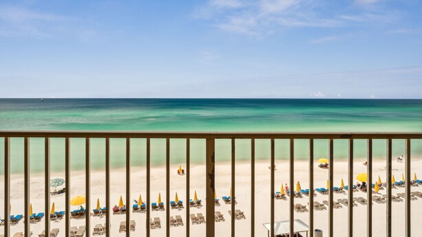 A beach view from a balcony with sun loungers and umbrellas.