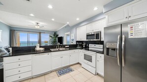 A modern kitchen with white cabinets, stainless steel appliances, and a view of the ocean.