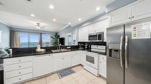 A modern kitchen with white cabinets, stainless steel appliances, and a view of the ocean.