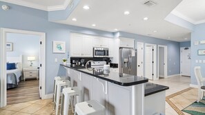 A modern kitchen with white cabinets, a black countertop, and a stainless steel refrigerator.