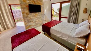 A hotel room with two beds, a stone wall, a TV, and a balcony with a view. - Jubaia Milagres by ER (São Miguel dos Milagres)