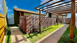 A courtyard with a pergola, a wooden fence, and a pathway leading to a building with a tiled roof. - Jubaia Milagres by ER (São Miguel dos Milagres)