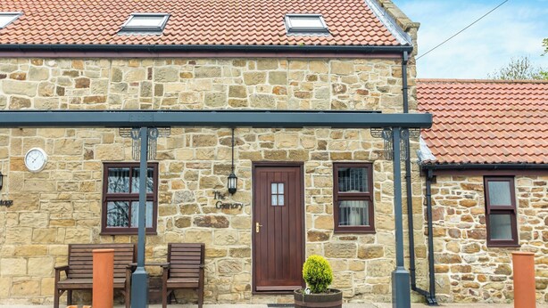 A stone building with a tiled roof, a wooden door, and a small garden area with a potted plant. - The Granary - UK43951 (Lingdale, near Saltburn-by-the-Sea)