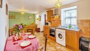 A compact kitchen with a dining area, a washing machine, and a window with blinds. - The Granary - UK43951 (Lingdale, near Saltburn-by-the-Sea)