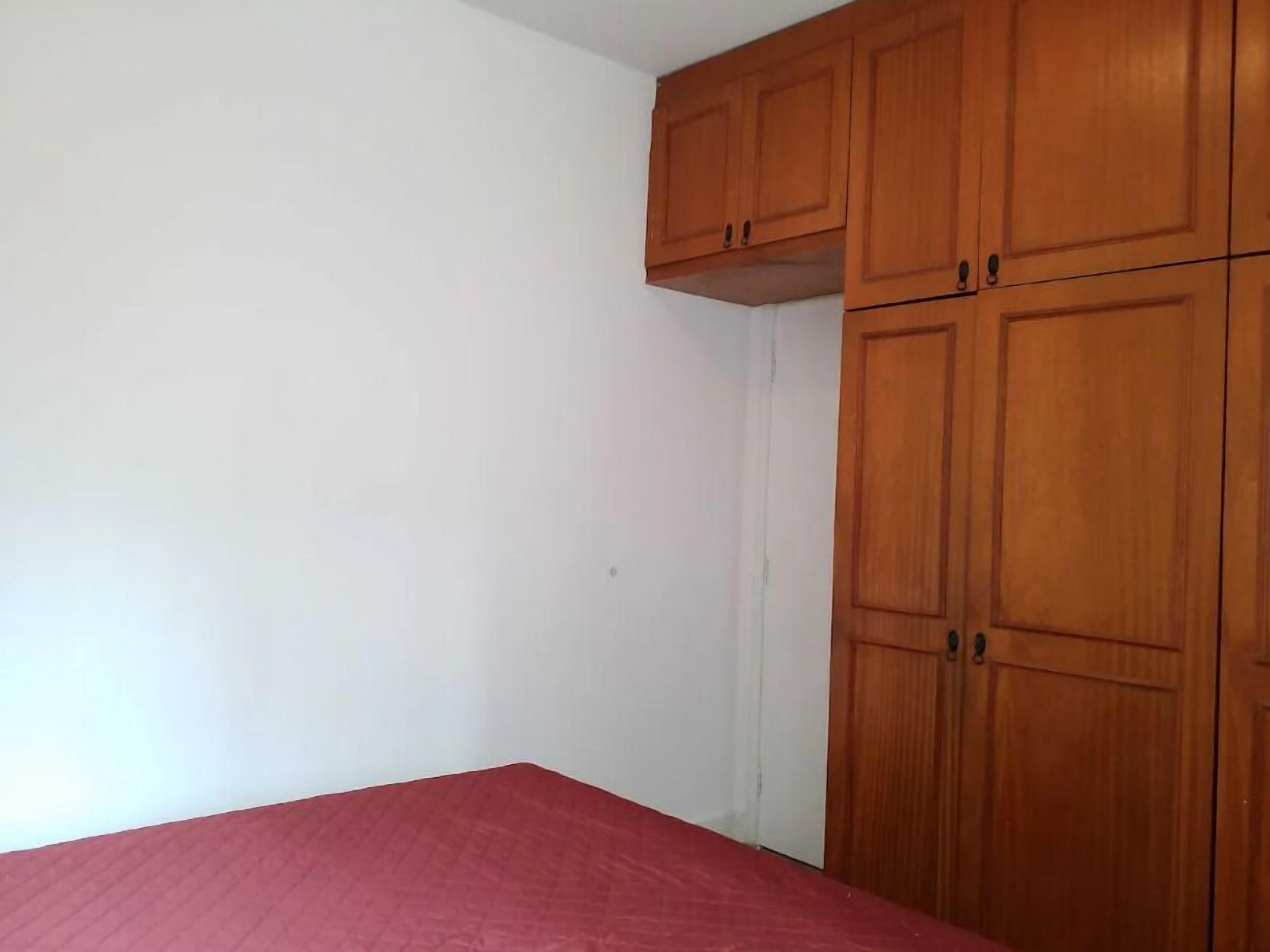 A bedroom with a red bedspread, white walls, and wooden cabinets.