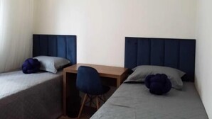 Ein kleiner, ordentlich eingerichteter Raum mit zwei Einzelbetten, einem Schreibtisch und einem Stuhl.
