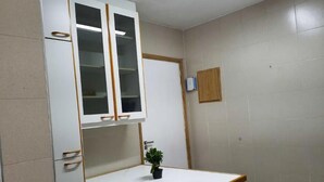 Ein kleiner Raum mit einem weißen Schrank, einem Tisch mit Stuhl und einer Topfpflanze.
