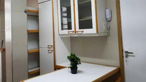 Ein kleiner, kompakter Raum mit einem weißen Tisch, einer Topfpflanze und einem Schrank mit Glastüren.