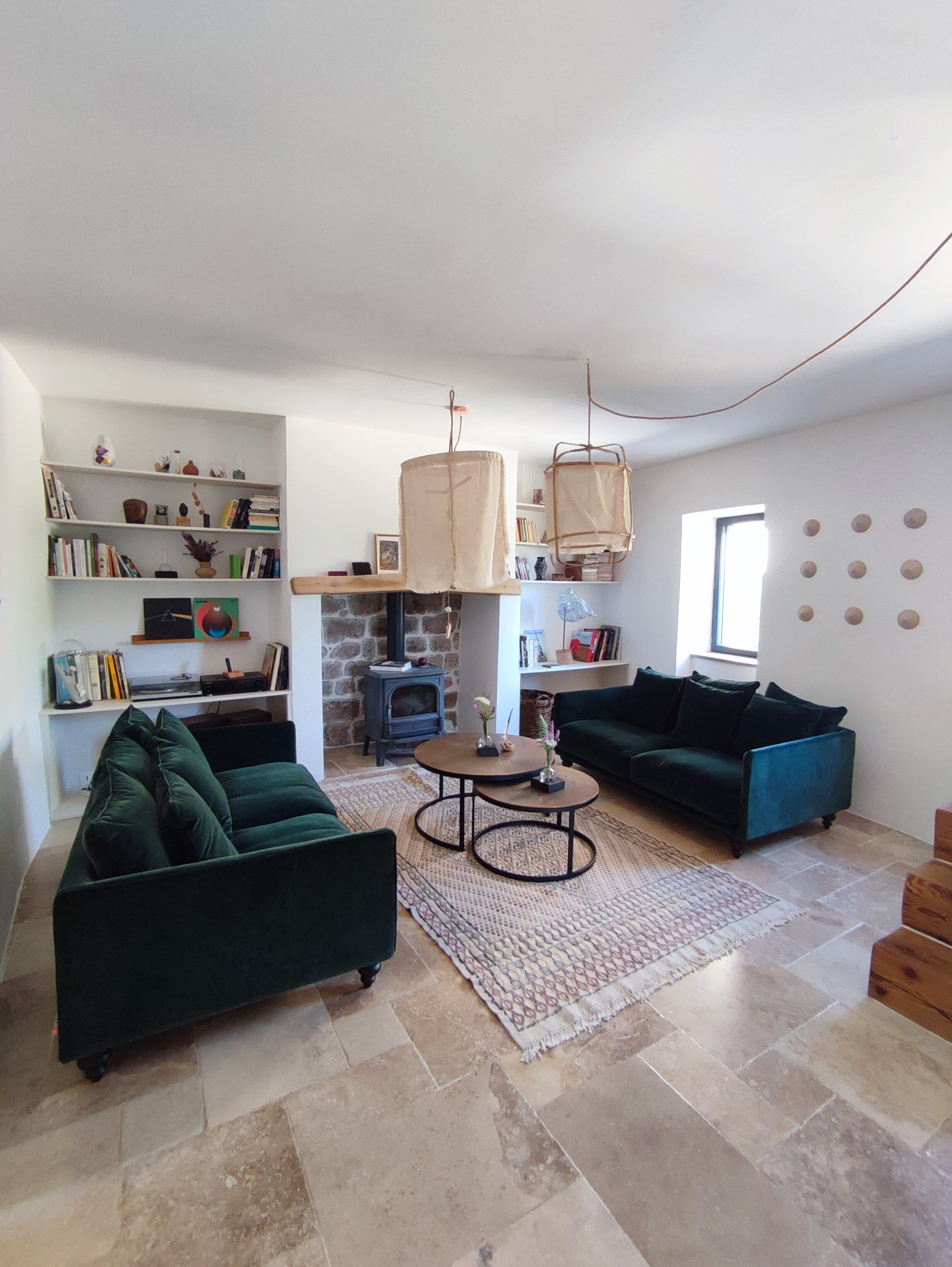 A living room with two green sofas, a round coffee table, a bookshelf, a stone fireplace, and a hanging light fixture.