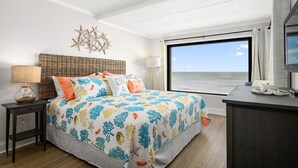 Ein Schlafzimmer mit einem großen Bett, einem Schreibtisch, einer Lampe und Meerblick.