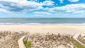 Ein Strand mit einem Sandweg, Dünen und freiem Blick auf den Ozean.