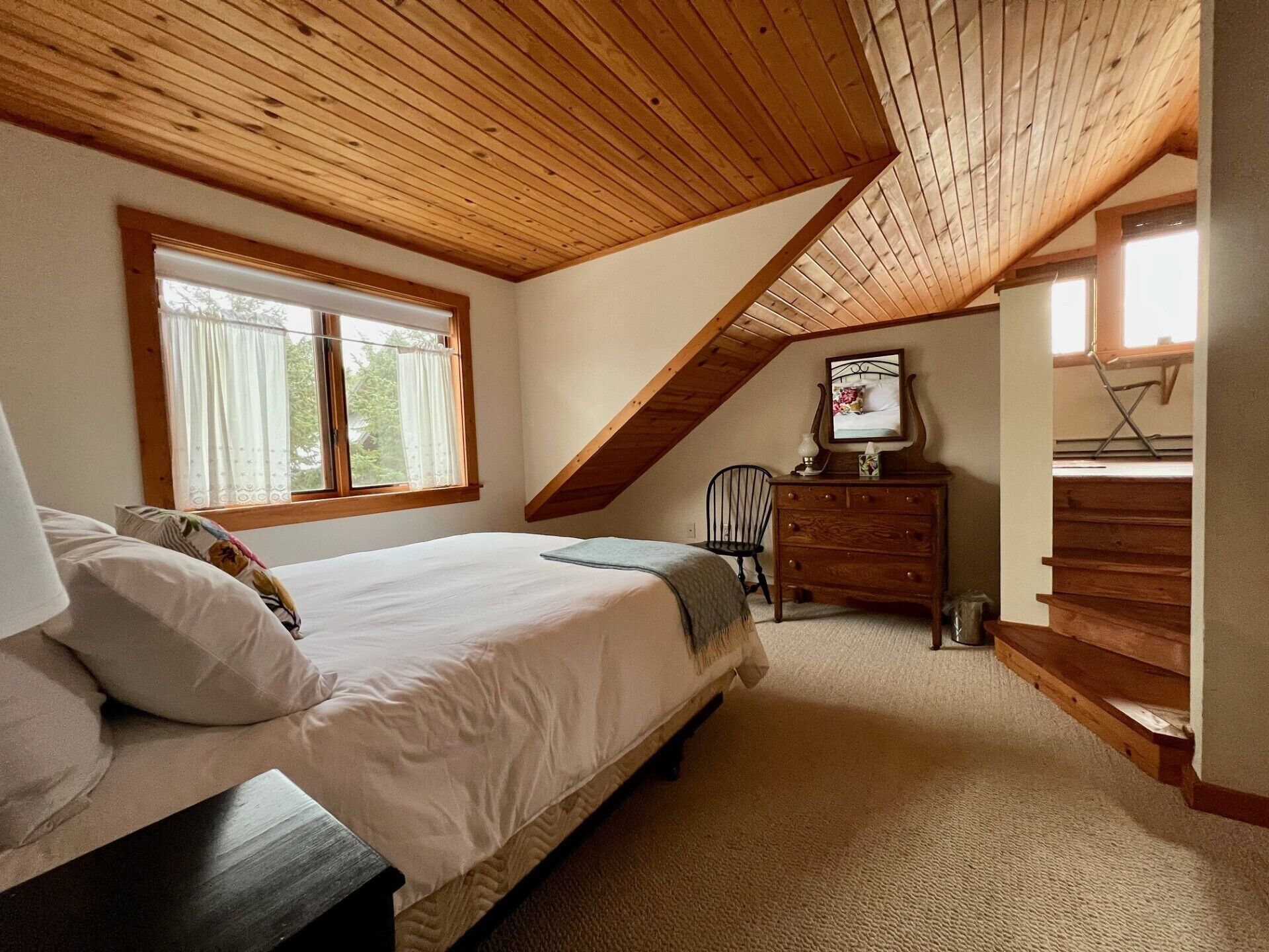 A bedroom with a sloped ceiling, a bed, a dresser, and a chair.