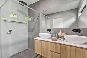A modern bathroom with a glass shower enclosure, two sinks, and a large mirror.