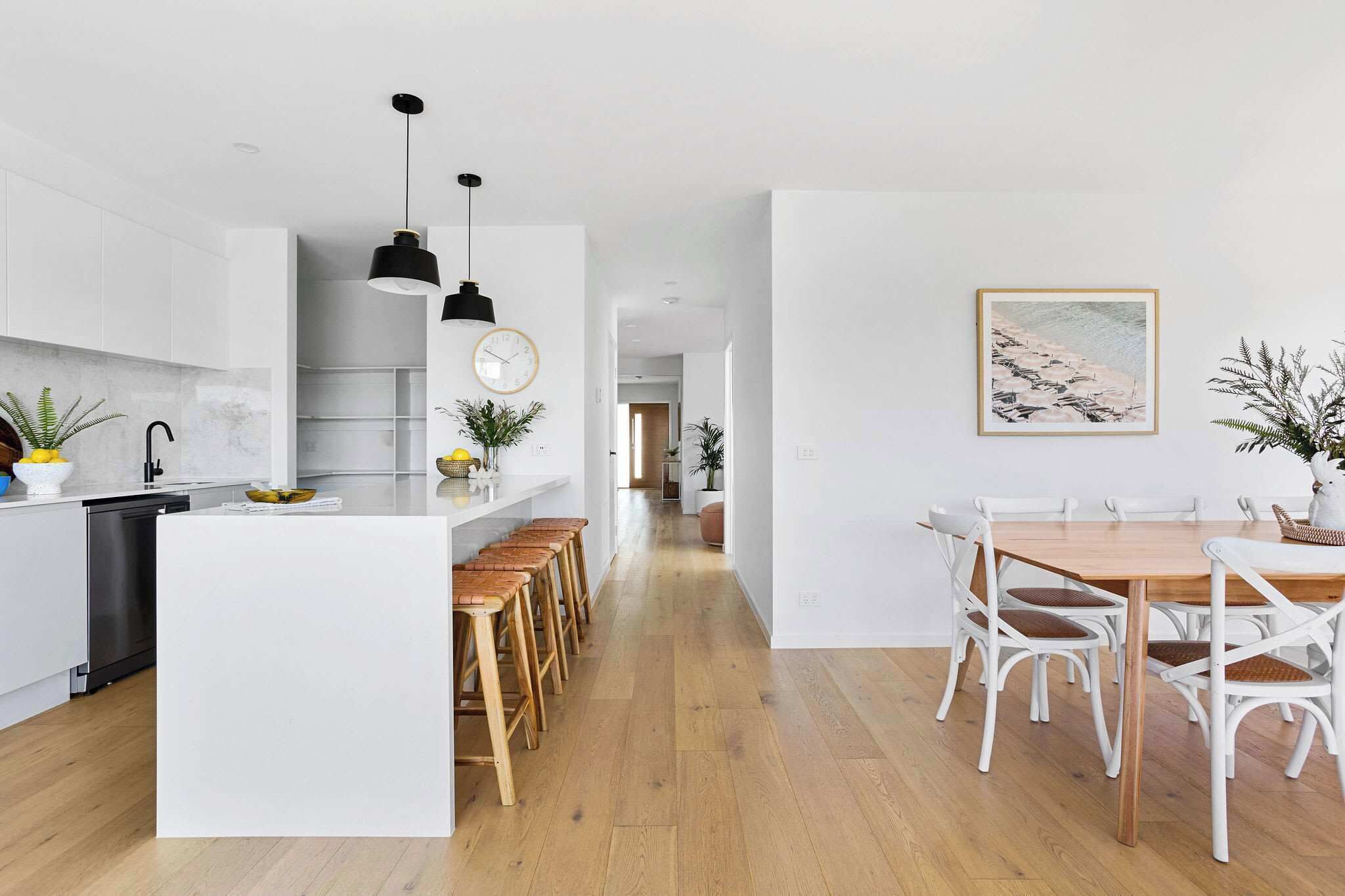 A modern kitchen with white cabinetry, a central island with stools, and a dining area with a wooden table and white chairs.