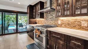 A modern kitchen with dark cabinetry, a stainless steel stove, and a glass-enclosed dining area. - Windward Escape (Pompano Beach)