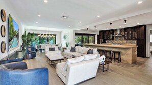 A spacious living area with a modern kitchen, white sofas, and a large window. - Windward Escape (Pompano Beach)