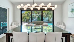 A modern dining area with a glass table, white chairs, a unique fish-shaped centerpiece, and a ceiling light fixture. - Windward Escape (Pompano Beach)