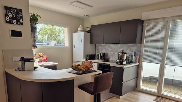 A modern kitchen with a curved island, dark cabinets, and a large window. - Bassin d'Arcachon: couple, quiet, bright, comfortable house with all amenities (Gujan-Mestras)