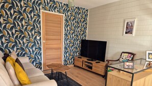A living room with a sofa, TV, wooden cabinet, and patterned wallpaper. - Bassin d'Arcachon: couple, quiet, bright, comfortable house with all amenities (Gujan-Mestras)