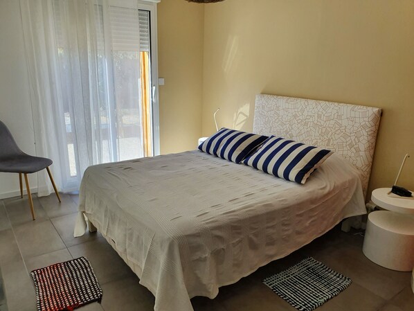 A bedroom with a bed, a chair, a bedside table, and a window with curtains.