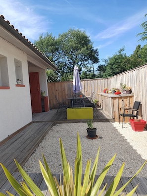 A backyard with a wooden deck, a yellow planter, a red chair, and a table with chairs.