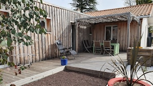 A wooden deck with a pergola, seating area, and a planter with a plant. - Bassin d'Arcachon: couple, quiet, bright, comfortable house with all amenities (Gujan-Mestras)