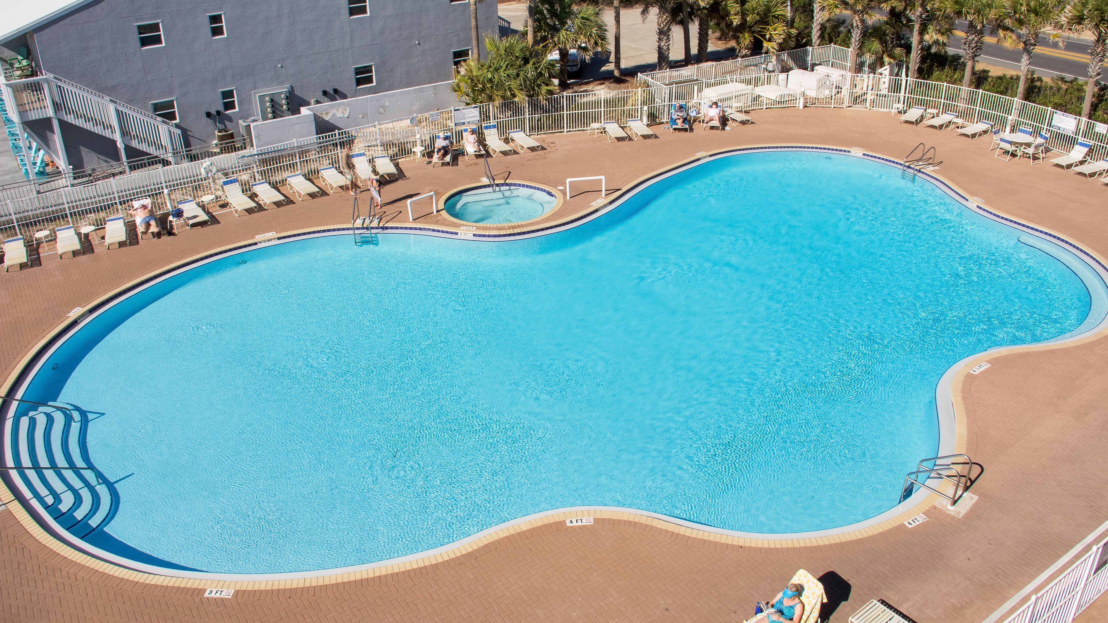 A large, oval-shaped swimming pool with a diving board, surrounded by lounge chairs and a fenced area.
