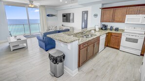 A modern kitchen with a large island, a dining area with a blue sofa, and a view of the ocean. - 1bd/2ba Unit w/ a Bunk Alcove and Amazing Views Right on the Gulf! (Panama City Beach)