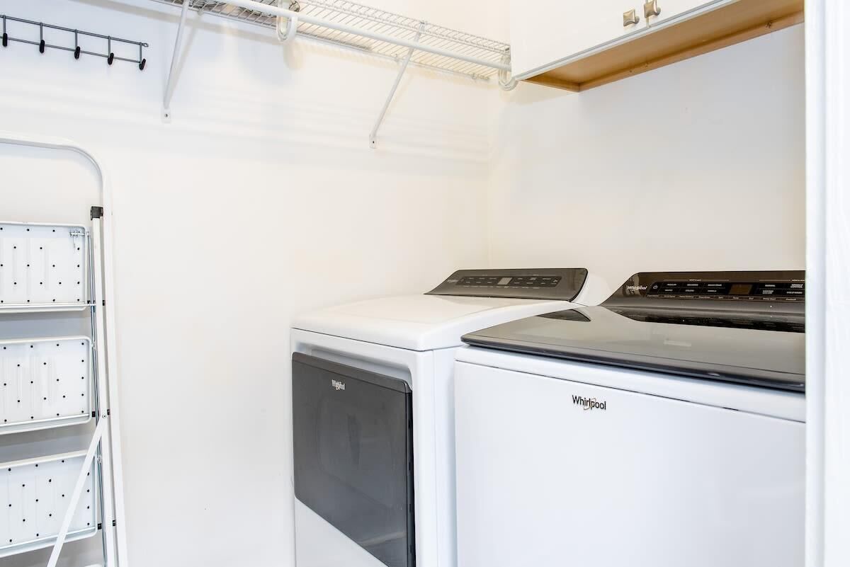 Ein Waschraum mit einer Whirlpool Waschmaschine und einem Trockner, einem Wäscheständer und einer weißen Wand.