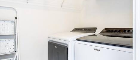 Ein Waschraum mit einer Whirlpool Waschmaschine und einem Trockner, einem Wäscheständer und einer weißen Wand.