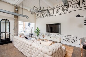 Un salon moderne avec un grand canapé beige, un téléviseur à écran plat et une fresque murale décorative.