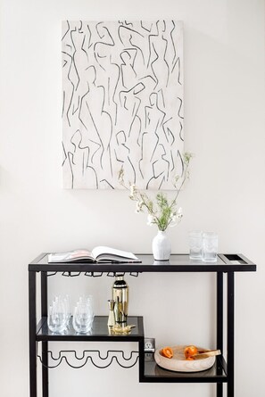 A modern room with a black console table, a white vase with flowers, a book, and a cocktail shaker.