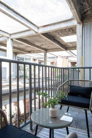 A balcony with a glass table, a potted plant, and a wicker chair with cushions. - Beltline Shrine (Atlanta)