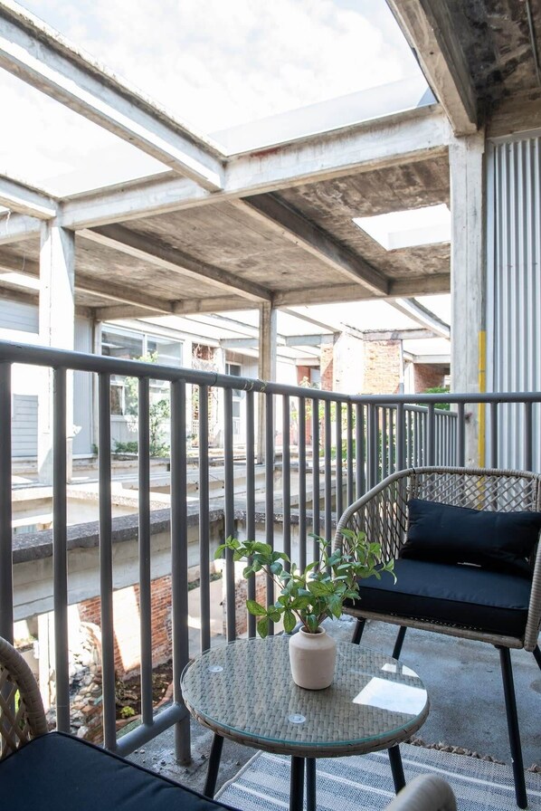 A balcony with a glass table, a potted plant, and a wicker chair with cushions.